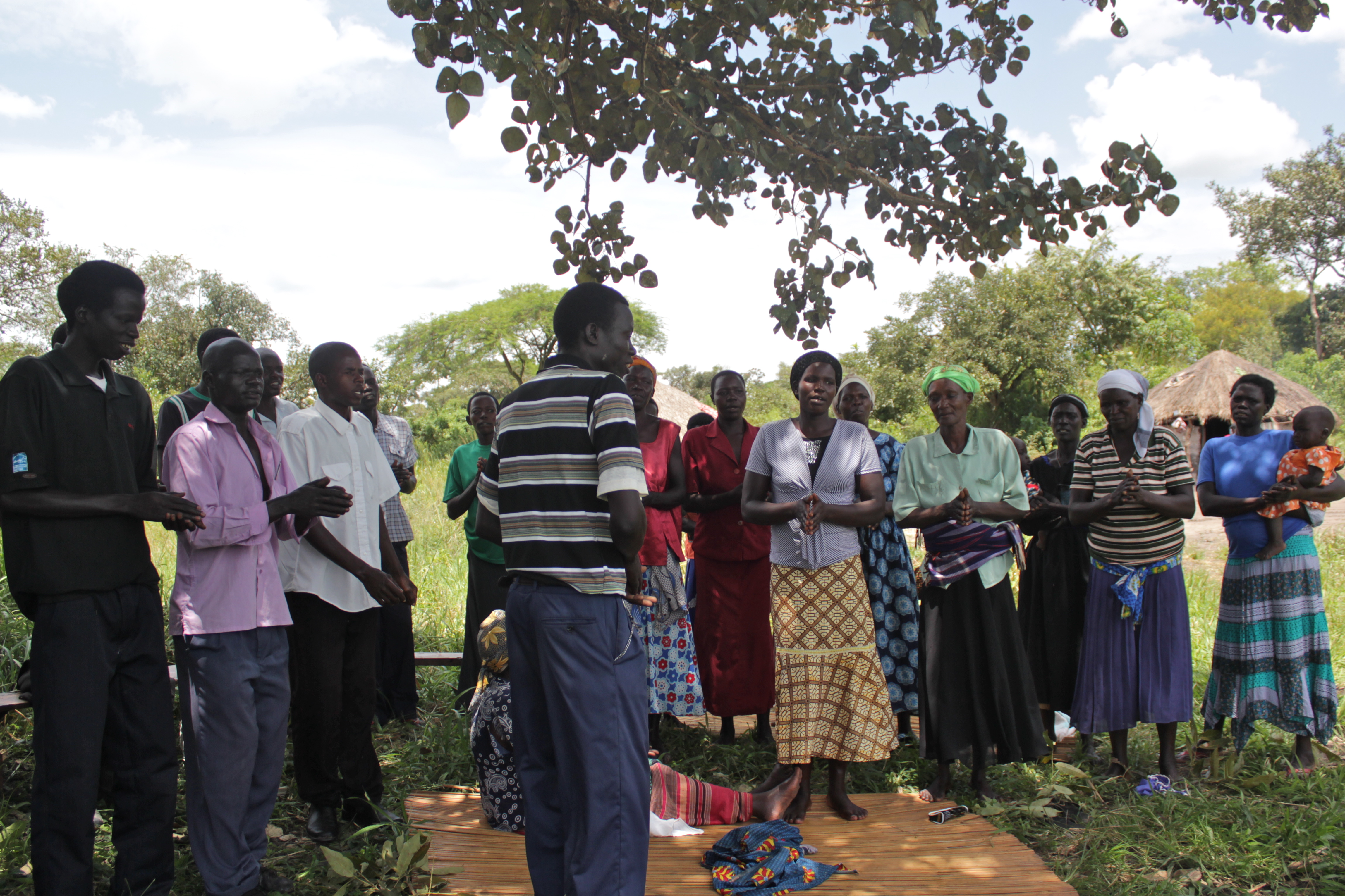 Moses (center, in stripes) leads his fellow members of his VSLA group in a song before beginning their action audit.