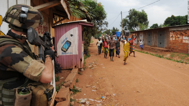 People walk by a French soldier standing guard during a disarmament operation in Bangui on December 9. (Photo credit: CNN)